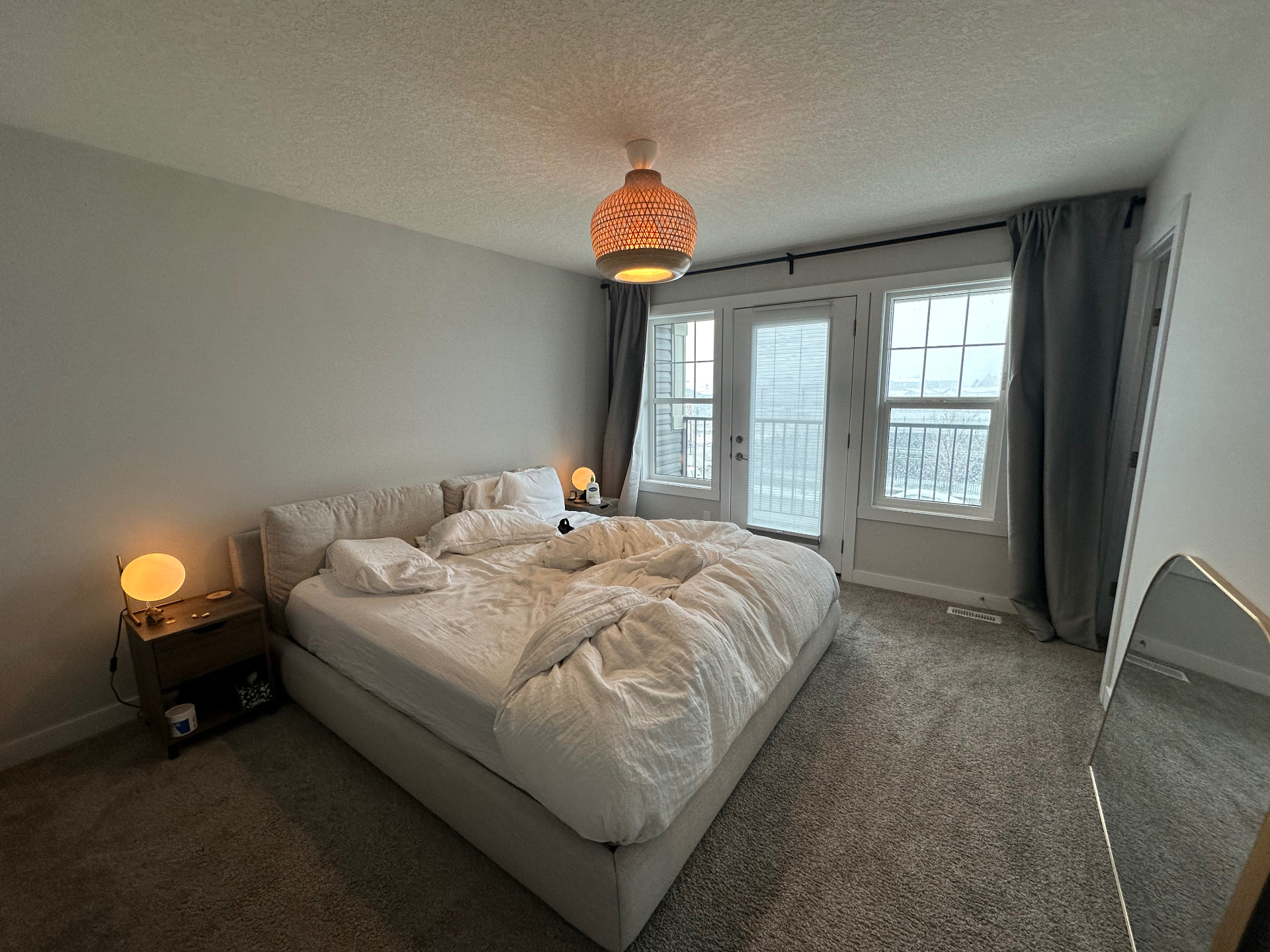 Original phone photo of a bedroom with unmade bed and warm ceiling light